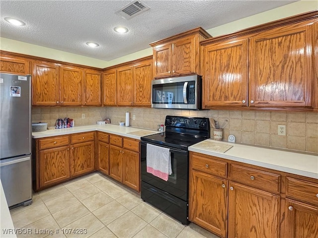 kitchen with a textured ceiling, decorative backsplash, light tile patterned floors, and stainless steel appliances