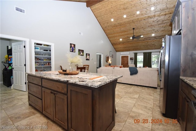 kitchen with high vaulted ceiling, a kitchen island, light stone countertops, and stainless steel refrigerator