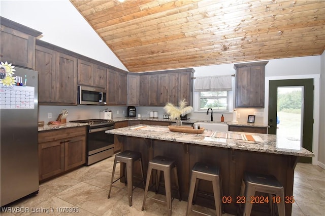 kitchen with sink, stainless steel appliances, light stone counters, lofted ceiling, and a breakfast bar area