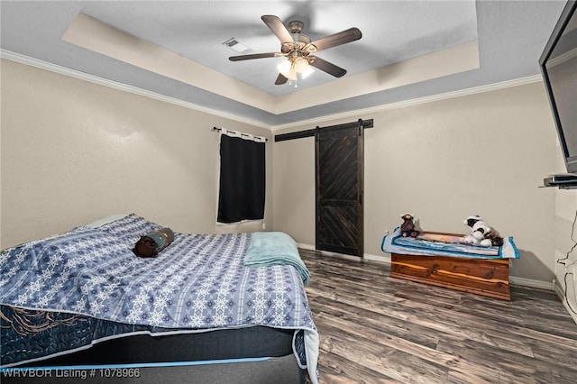 bedroom featuring crown molding, a tray ceiling, dark wood-type flooring, and a barn door