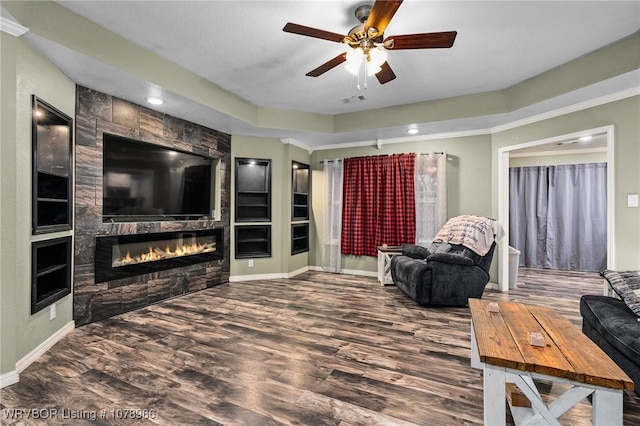 living room with hardwood / wood-style floors, a fireplace, ornamental molding, ceiling fan, and a tray ceiling