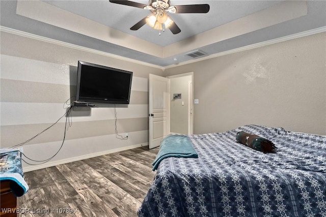 bedroom with dark hardwood / wood-style floors, ceiling fan, ornamental molding, and a tray ceiling