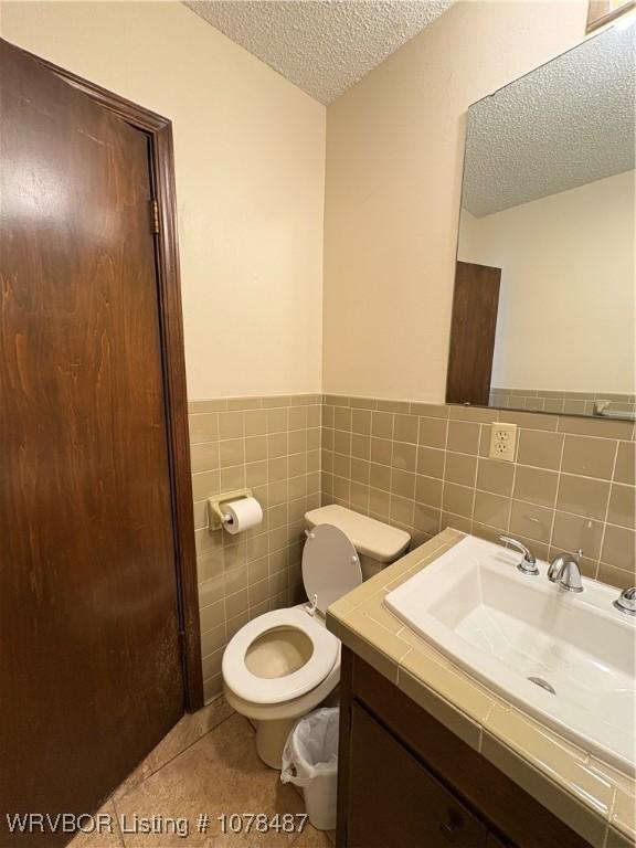 bathroom featuring vanity, toilet, a textured ceiling, and tile walls