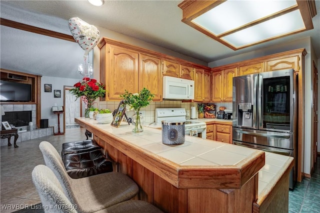 kitchen featuring white appliances, decorative backsplash, tile countertops, a peninsula, and a fireplace