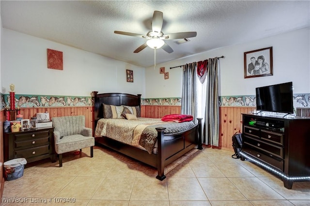 bedroom with visible vents, wainscoting, wood walls, a textured ceiling, and light tile patterned flooring