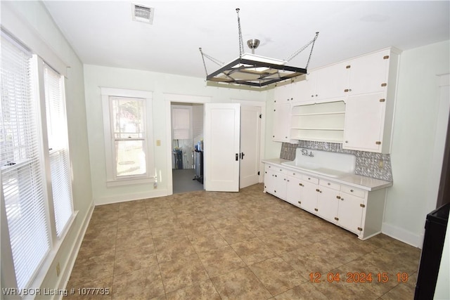 kitchen with backsplash, white cabinetry, and decorative light fixtures