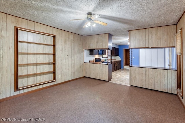 kitchen with light brown cabinetry, a textured ceiling, ceiling fan, and wooden walls