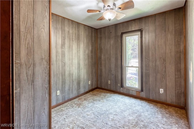 carpeted empty room with ceiling fan, wooden walls, and a textured ceiling