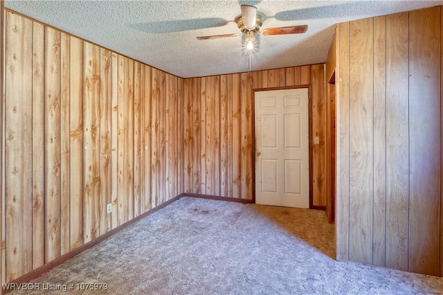 empty room featuring ceiling fan, wood walls, carpet floors, and a textured ceiling