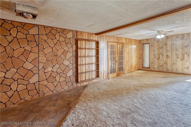 carpeted spare room featuring beamed ceiling, ceiling fan, a textured ceiling, and wooden walls