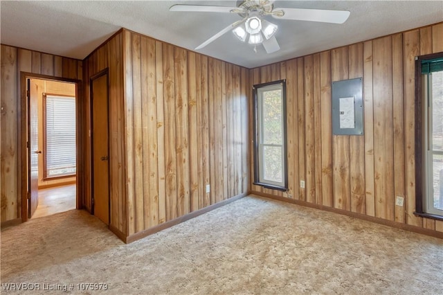 unfurnished room featuring wood walls, light carpet, electric panel, ceiling fan, and a textured ceiling