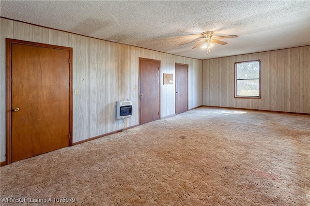 unfurnished bedroom featuring a textured ceiling, heating unit, light colored carpet, ceiling fan, and multiple closets