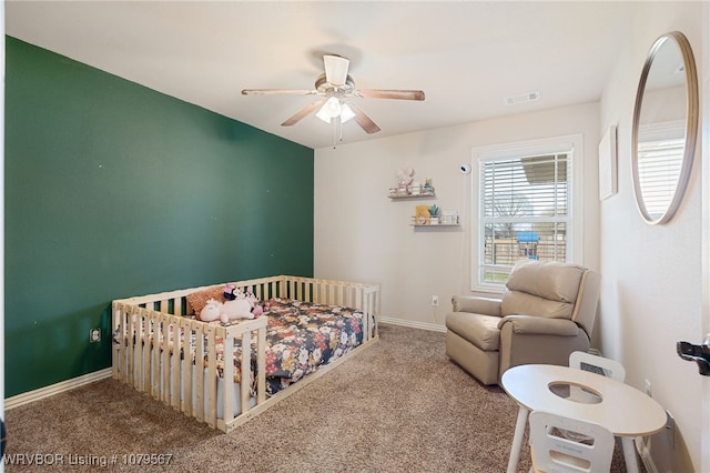 carpeted bedroom with visible vents, baseboards, a nursery area, and ceiling fan