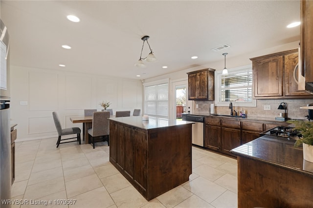 kitchen with dark countertops, visible vents, backsplash, dishwasher, and a decorative wall