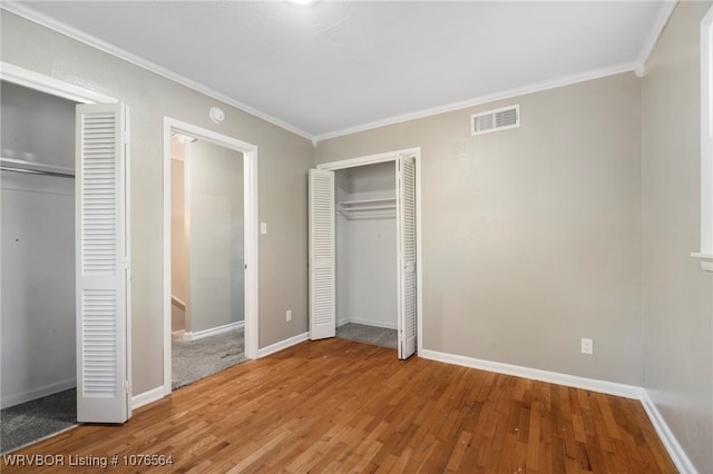 unfurnished bedroom with multiple closets, wood-type flooring, and ornamental molding