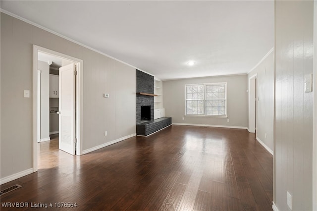 unfurnished living room with built in shelves, dark wood-type flooring, a brick fireplace, crown molding, and wooden walls