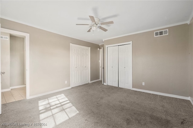 unfurnished bedroom featuring multiple closets, ceiling fan, crown molding, and light carpet