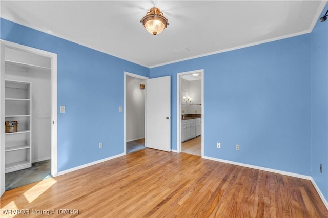 unfurnished bedroom featuring baseboards, ensuite bath, light wood-style flooring, and ornamental molding