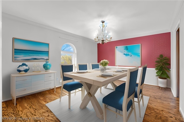 dining space with light wood-type flooring, an inviting chandelier, crown molding, baseboards, and an accent wall