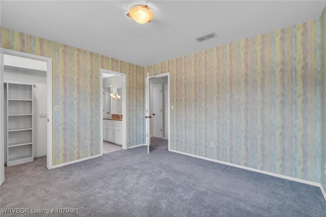 unfurnished bedroom with wallpapered walls, a walk in closet, and carpet floors