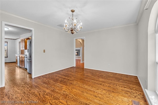 empty room with wood finished floors, visible vents, baseboards, an inviting chandelier, and crown molding