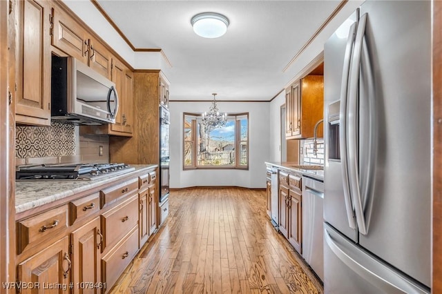 kitchen with ornamental molding, decorative backsplash, light wood-style floors, stainless steel appliances, and a sink