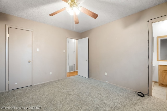 unfurnished bedroom with ensuite bathroom, light colored carpet, ceiling fan, and a textured ceiling