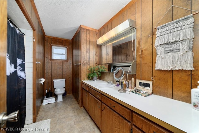 bathroom with vanity, wood walls, toilet, and a textured ceiling