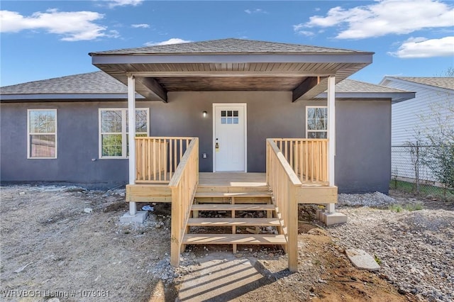 doorway to property with roof with shingles, fence, and stucco siding