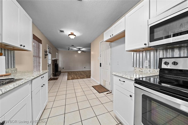 kitchen with stainless steel appliances, light tile patterned floors, white cabinets, and light stone counters