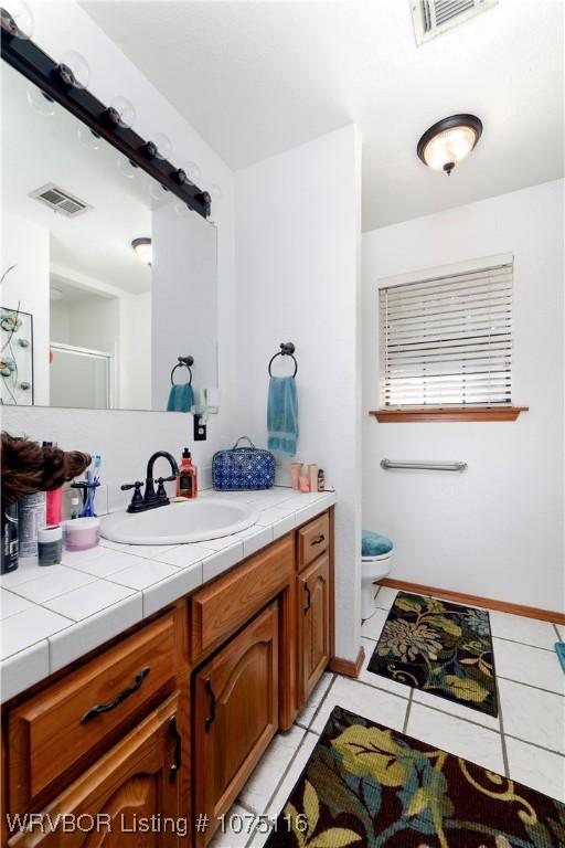 bathroom with tile patterned flooring, vanity, a shower with shower door, and toilet