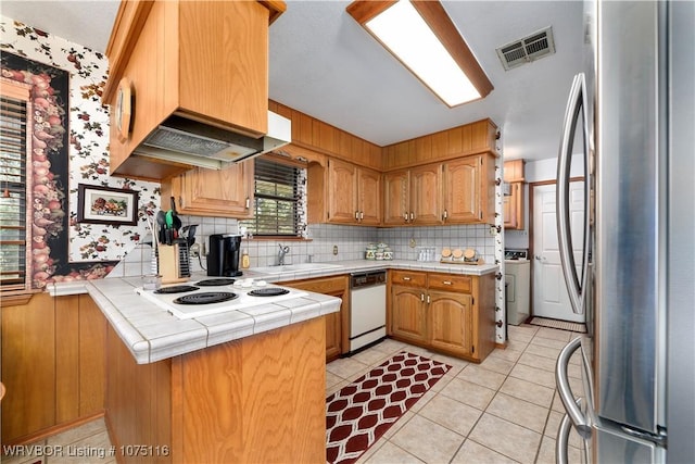 kitchen with tile countertops, premium range hood, white dishwasher, stainless steel fridge, and kitchen peninsula