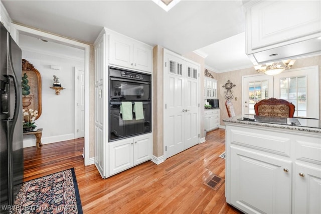 kitchen with light stone counters, ornamental molding, black appliances, white cabinets, and light wood-type flooring