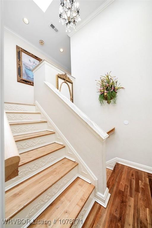 stairs featuring hardwood / wood-style flooring, ornamental molding, and an inviting chandelier