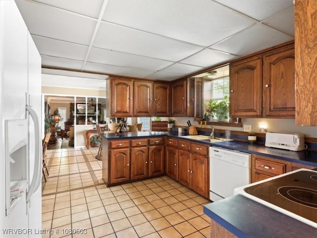kitchen with a paneled ceiling, a sink, light tile patterned floors, white appliances, and dark countertops