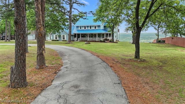 view of front of property with a porch, a front yard, metal roof, a water view, and aphalt driveway