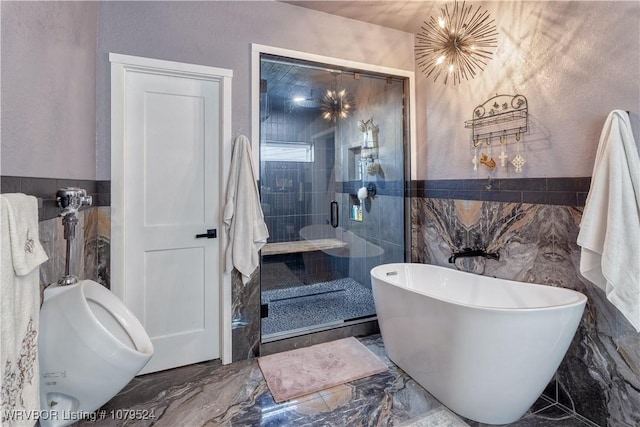 full bathroom featuring a freestanding tub, marble finish floor, a stall shower, tile walls, and a chandelier