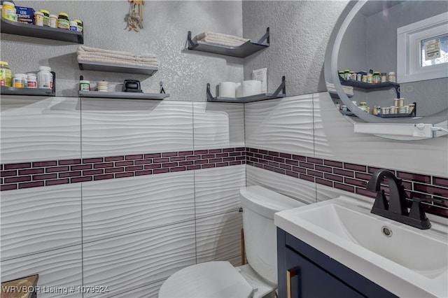 bathroom featuring vanity, toilet, a textured wall, and backsplash