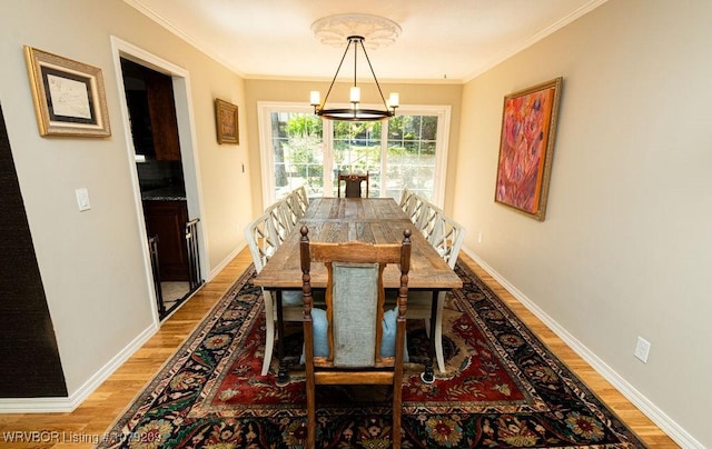 dining area featuring ornamental molding, light wood finished floors, a notable chandelier, and baseboards