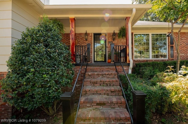 view of exterior entry featuring covered porch and brick siding