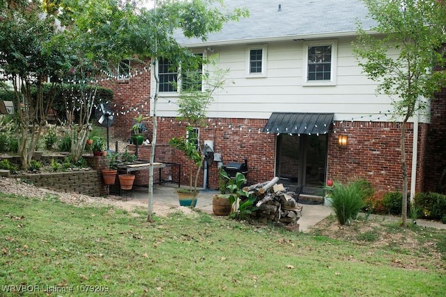 rear view of house with a yard, a patio area, brick siding, and roof with shingles