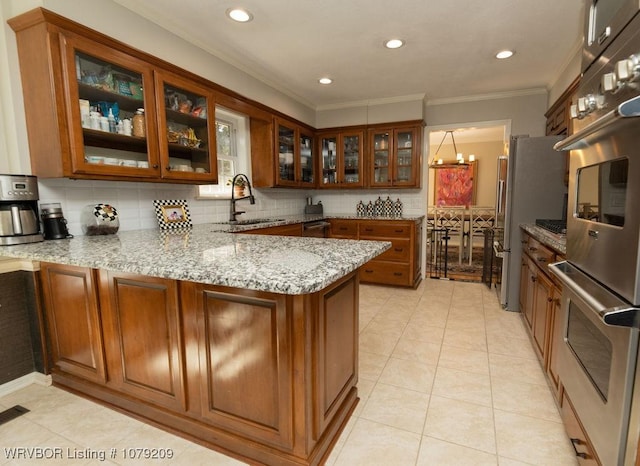 kitchen featuring light stone countertops, a peninsula, a sink, brown cabinets, and glass insert cabinets