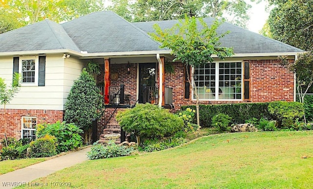 view of front of property featuring covered porch, brick siding, a front lawn, and a shingled roof