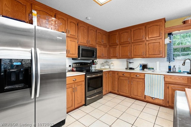 kitchen with tasteful backsplash, a textured ceiling, stainless steel appliances, sink, and light tile patterned floors