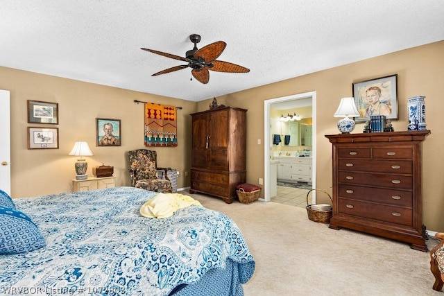 bedroom featuring ceiling fan, light colored carpet, a textured ceiling, and ensuite bath