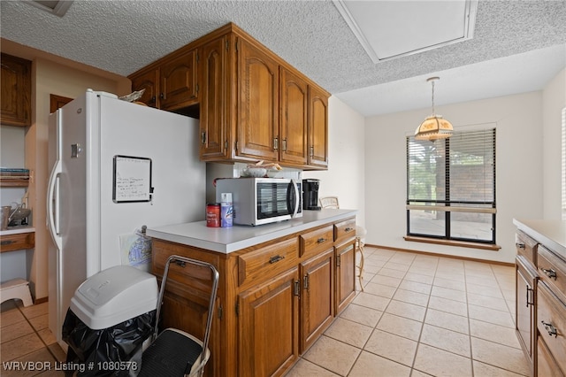 kitchen with a textured ceiling, stainless steel microwave, brown cabinets, light tile patterned floors, and light countertops