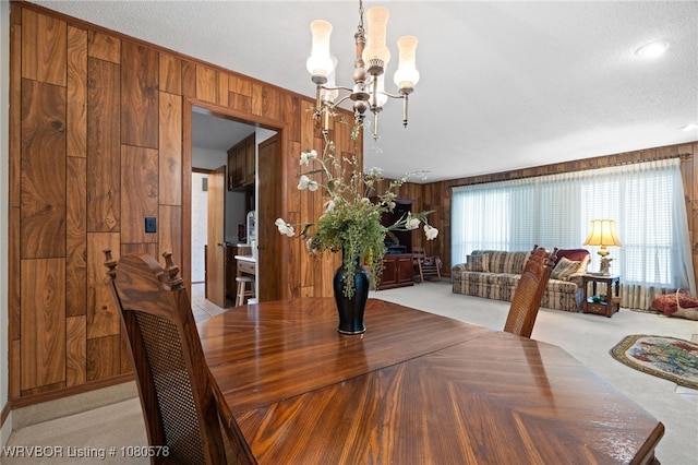 dining room featuring an inviting chandelier, a textured ceiling, wooden walls, and light carpet