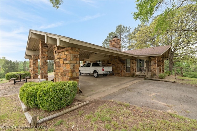 exterior space with a carport, stone siding, aphalt driveway, and a chimney