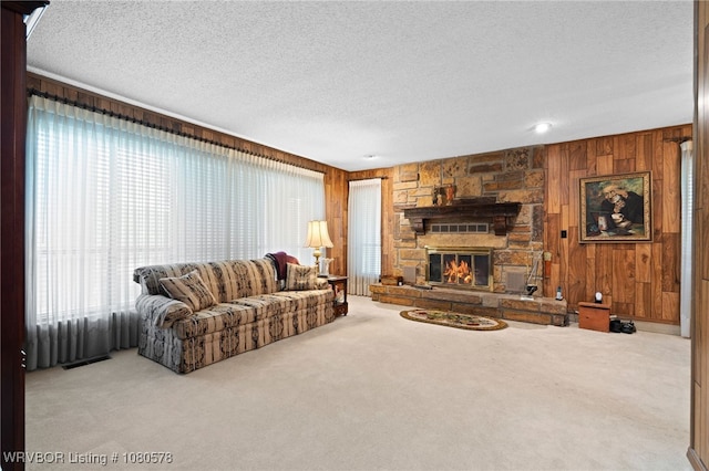 carpeted living area with a textured ceiling, a stone fireplace, wood walls, and visible vents