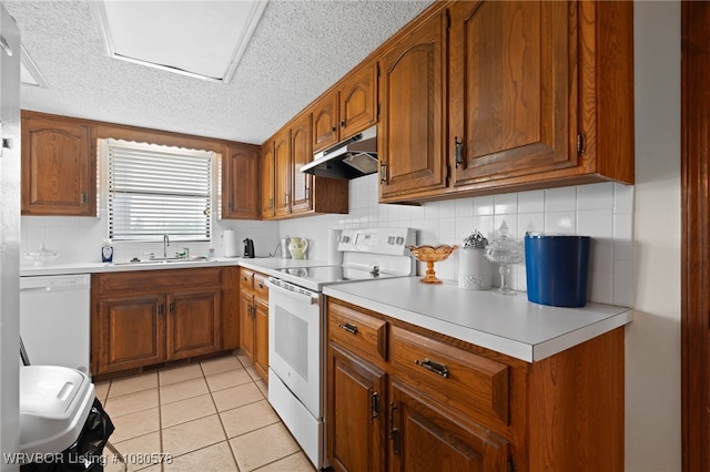 kitchen featuring white appliances, a textured ceiling, under cabinet range hood, and brown cabinets